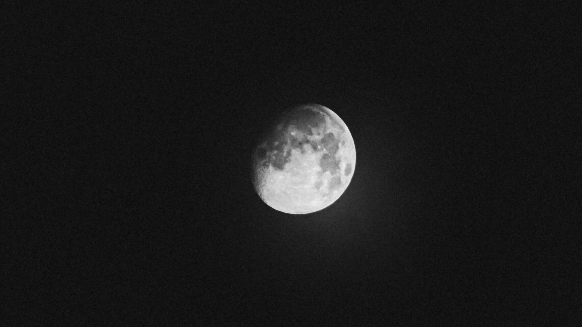 From below of black and white moon in waxing gibbous lunar phase shining in dark night sky